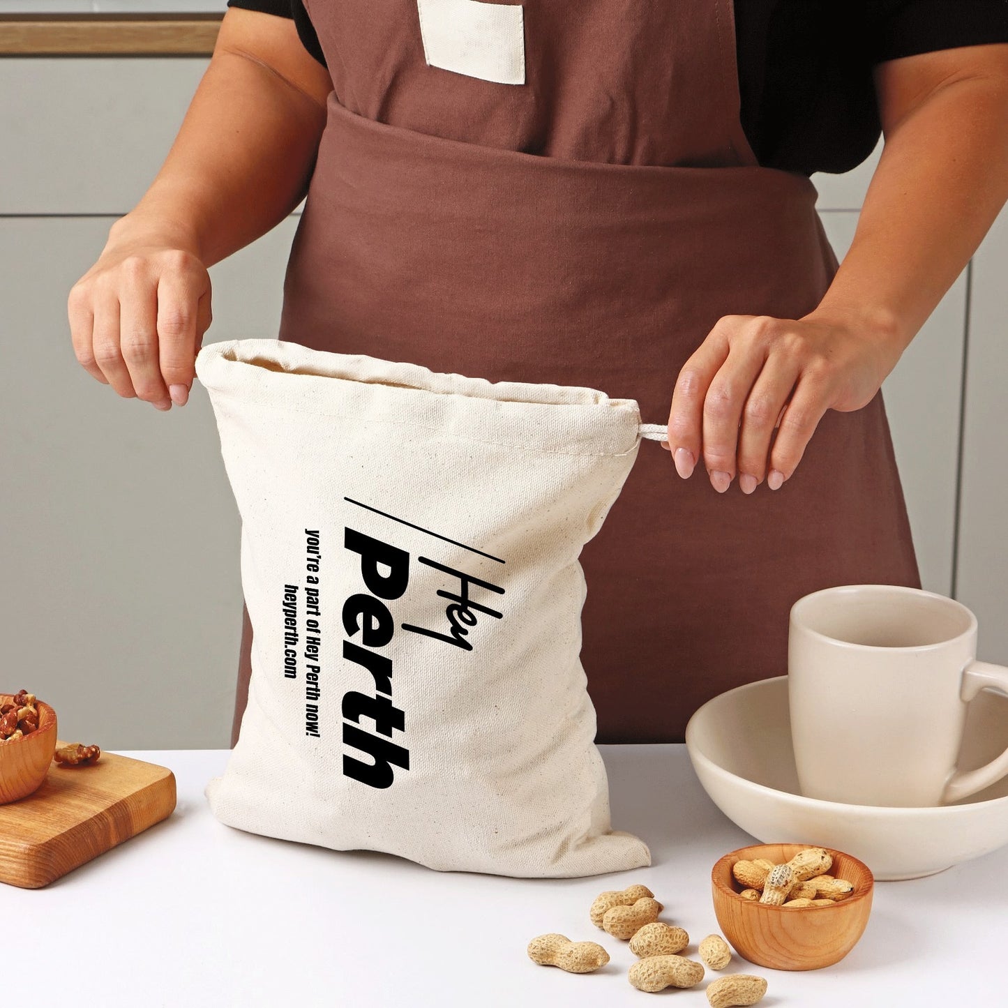 Person wearing a brown apron with a 'Hey Perth' bag in a kitchen setting.