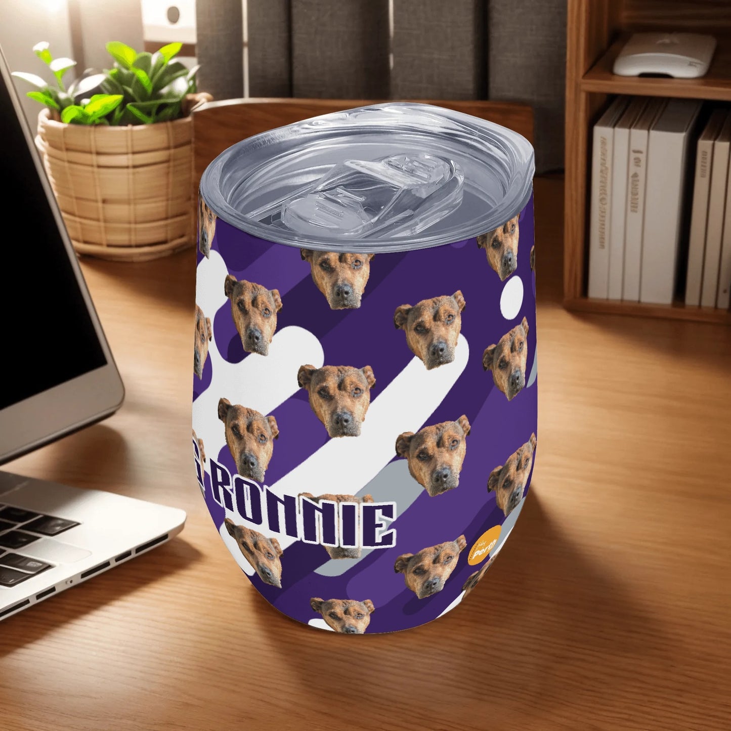 Wine tumbler with dog pattern and on a desk with laptop and books.