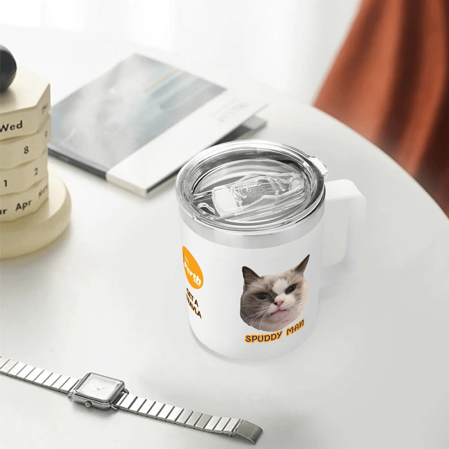 White tumbler with a cat design and text on a white surface with a watch and calendar in the background.